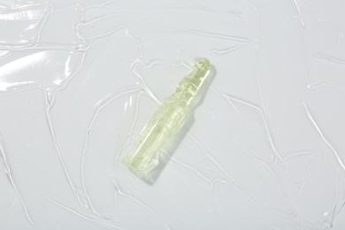 Skincare ampoule on white surface covered with gel, top view