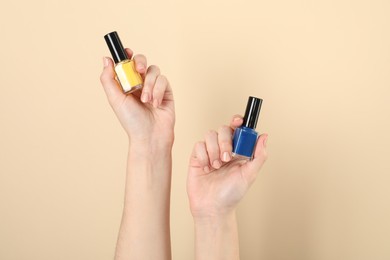 Photo of Woman holding nail polishes on beige background, closeup