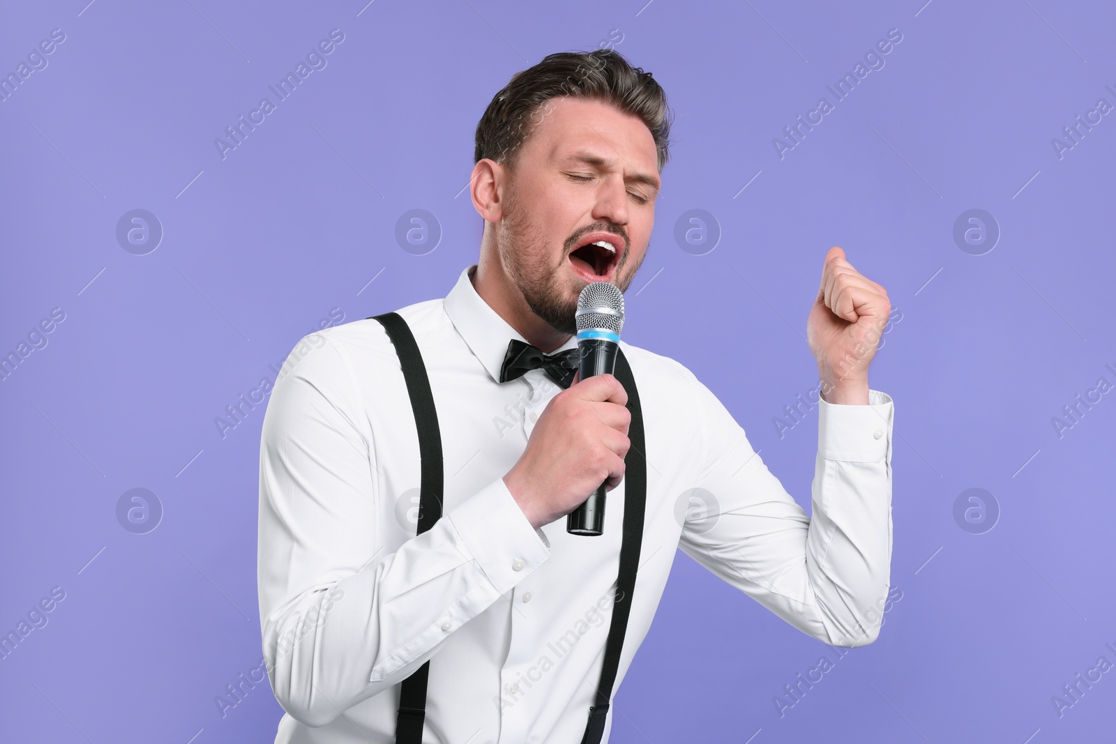 Photo of Handsome man with microphone singing on violet background