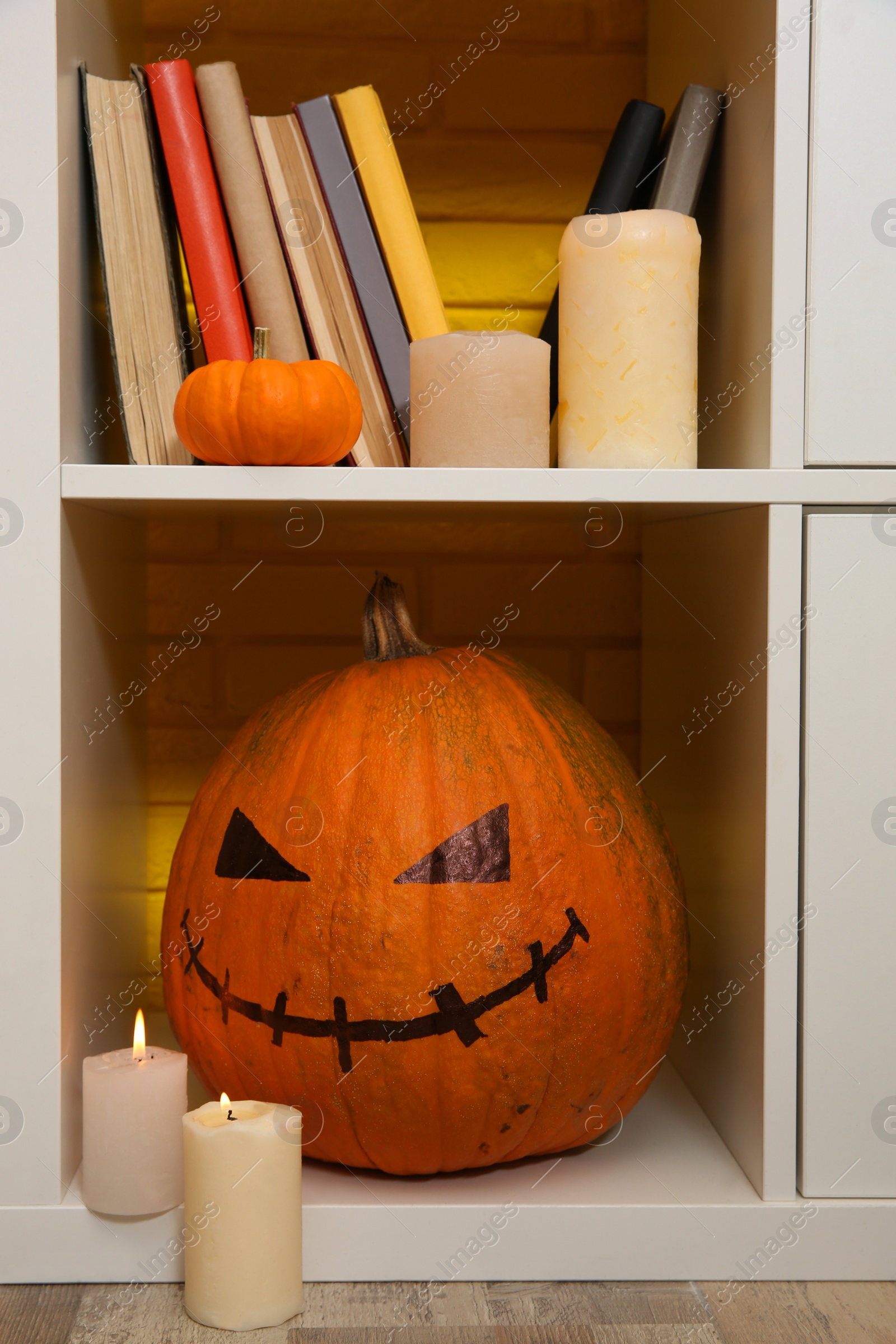 Photo of Pumpkin with drawn spooky face and candles on shelf. Halloween decor