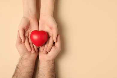 Couple holding red heart on beige background, top view. Space for text