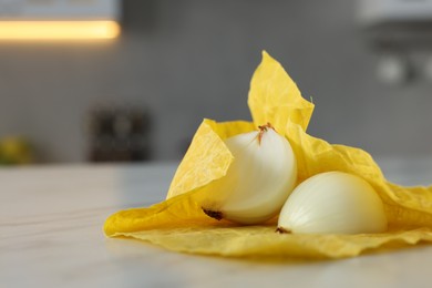 Halves of onion with yellow beeswax food wrap on white table, closeup. Space for text