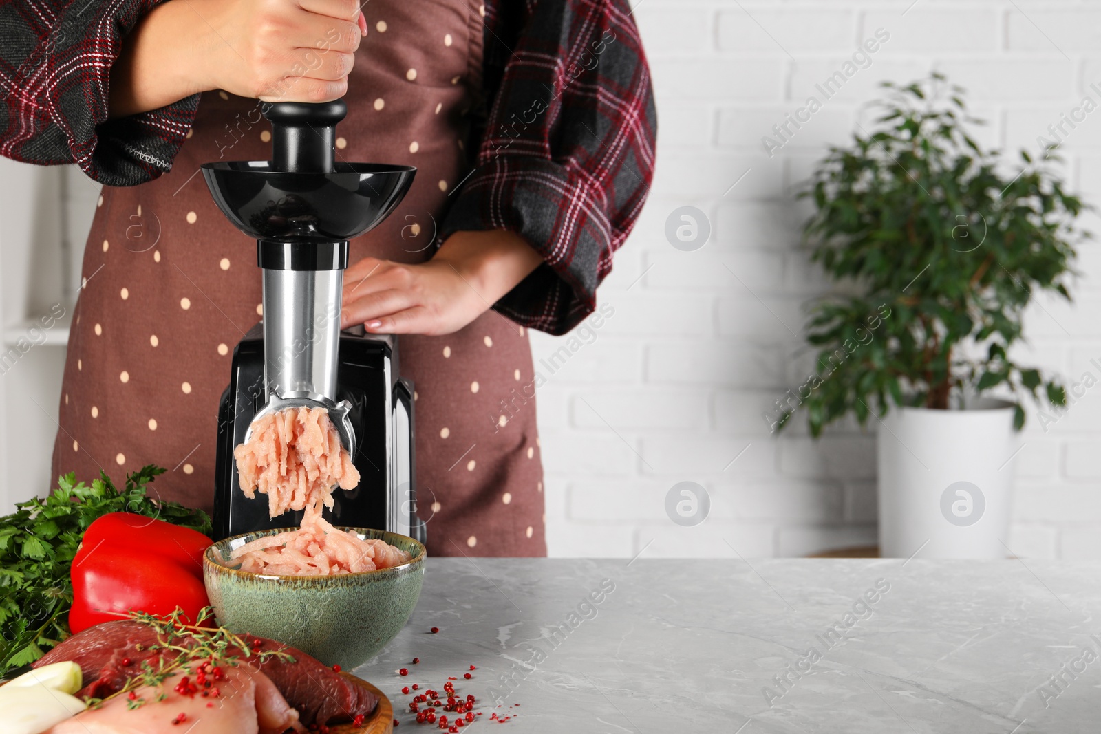 Photo of Woman making chicken mince with electric meat grinder at grey marble table indoors, closeup. Space for text