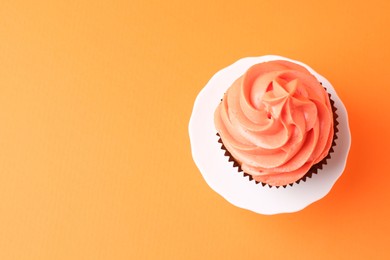 Delicious cupcake with bright cream on orange background, top view. Space for text