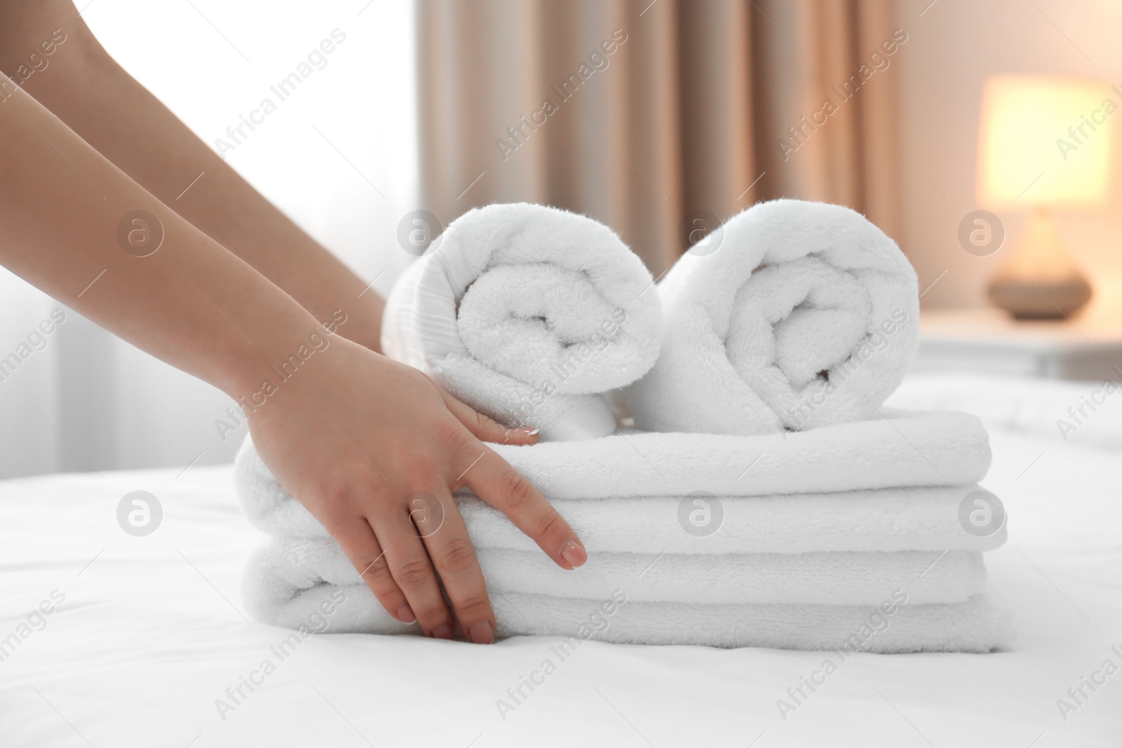 Photo of Chambermaid with stack of towels on bed in hotel room