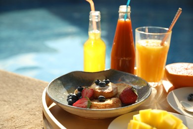 Photo of Tray with delicious breakfast near swimming pool, closeup