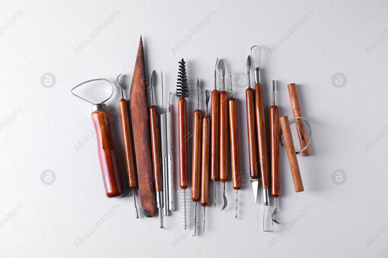 Photo of Set of different clay crafting tools on white textured table, flat lay