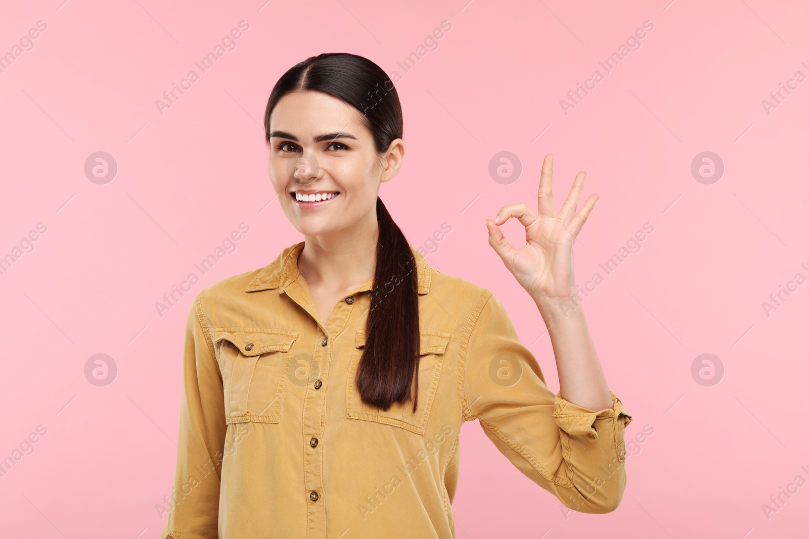 Photo of Young woman with clean teeth smiling and showing ok gesture on pink background