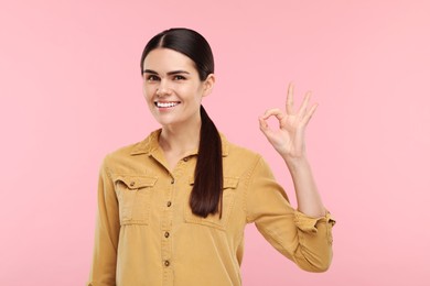 Photo of Young woman with clean teeth smiling and showing ok gesture on pink background