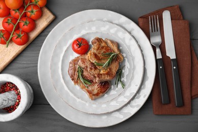 Photo of Delicious fried meat with rosemary and tomato served on grey wooden table, flat lay