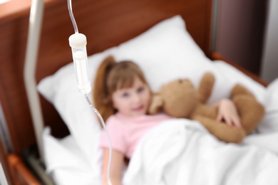 Photo of Little child with intravenous infusion and toy in hospital bed, focus on drip chamber