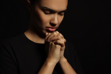 African American woman with clasped hands praying to God on black background. Space for text