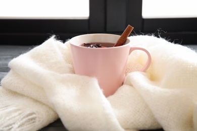 Photo of Cup of hot winter drink with knitted scarf near window. Cozy season