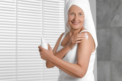 Happy woman applying body cream onto shoulder indoors. Space for text