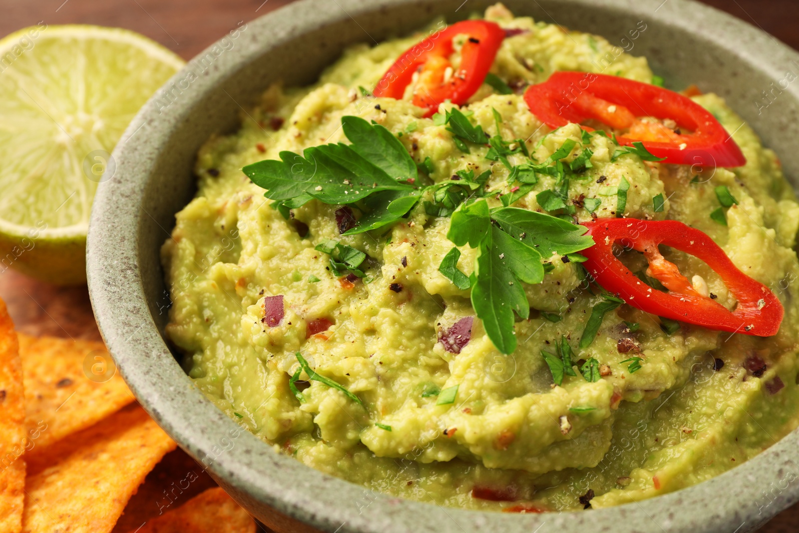 Photo of Bowl of delicious guacamole, lime and tortilla chips, closeup