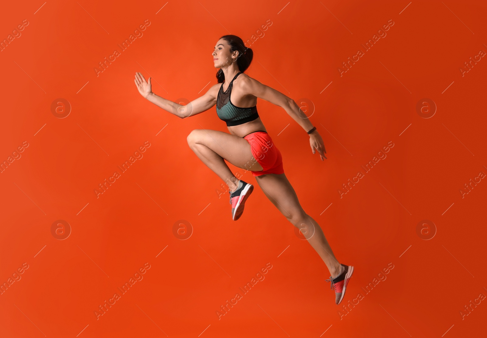 Photo of Athletic young woman running on red background, side view