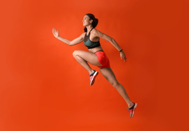 Photo of Athletic young woman running on red background, side view