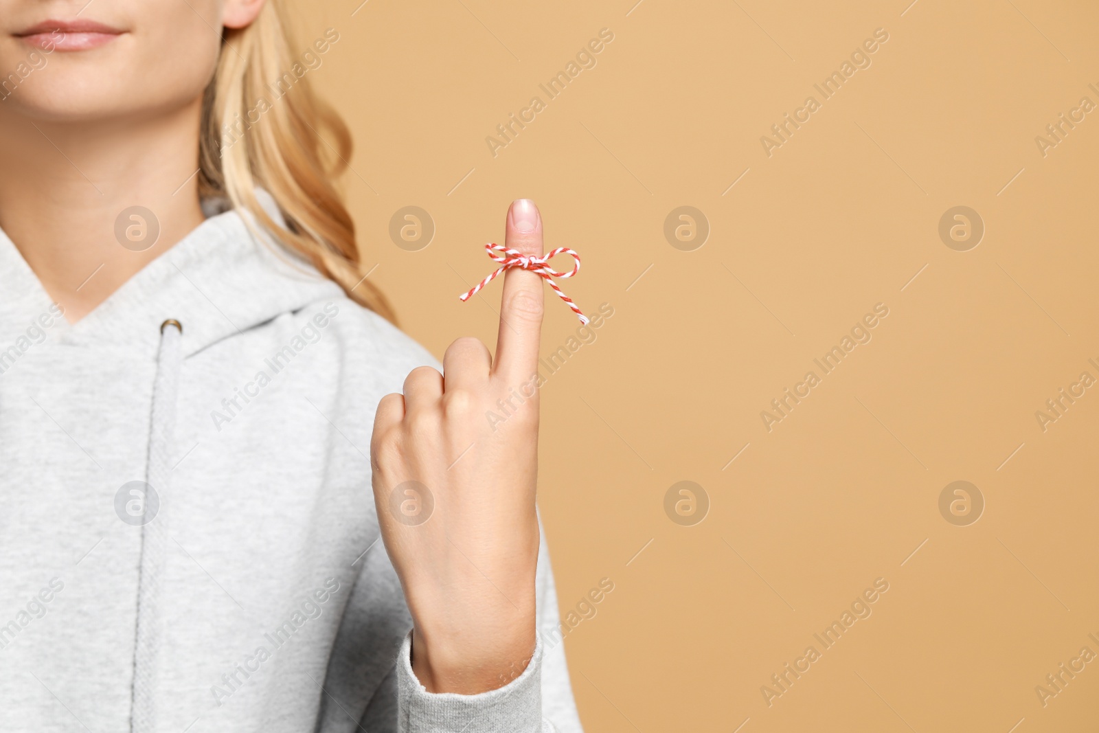 Photo of Woman showing index finger with tied bow as reminder on light brown background, closeup. Space for text