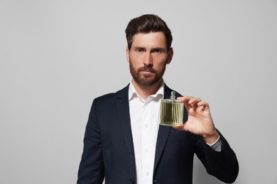 Photo of Handsome bearded man with bottle of perfume on light grey background