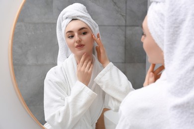 Photo of Beautiful woman wearing white robe and looking in mirror in bathroom