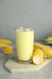 Photo of Tasty fresh corn milk in glass and cobs on light grey table
