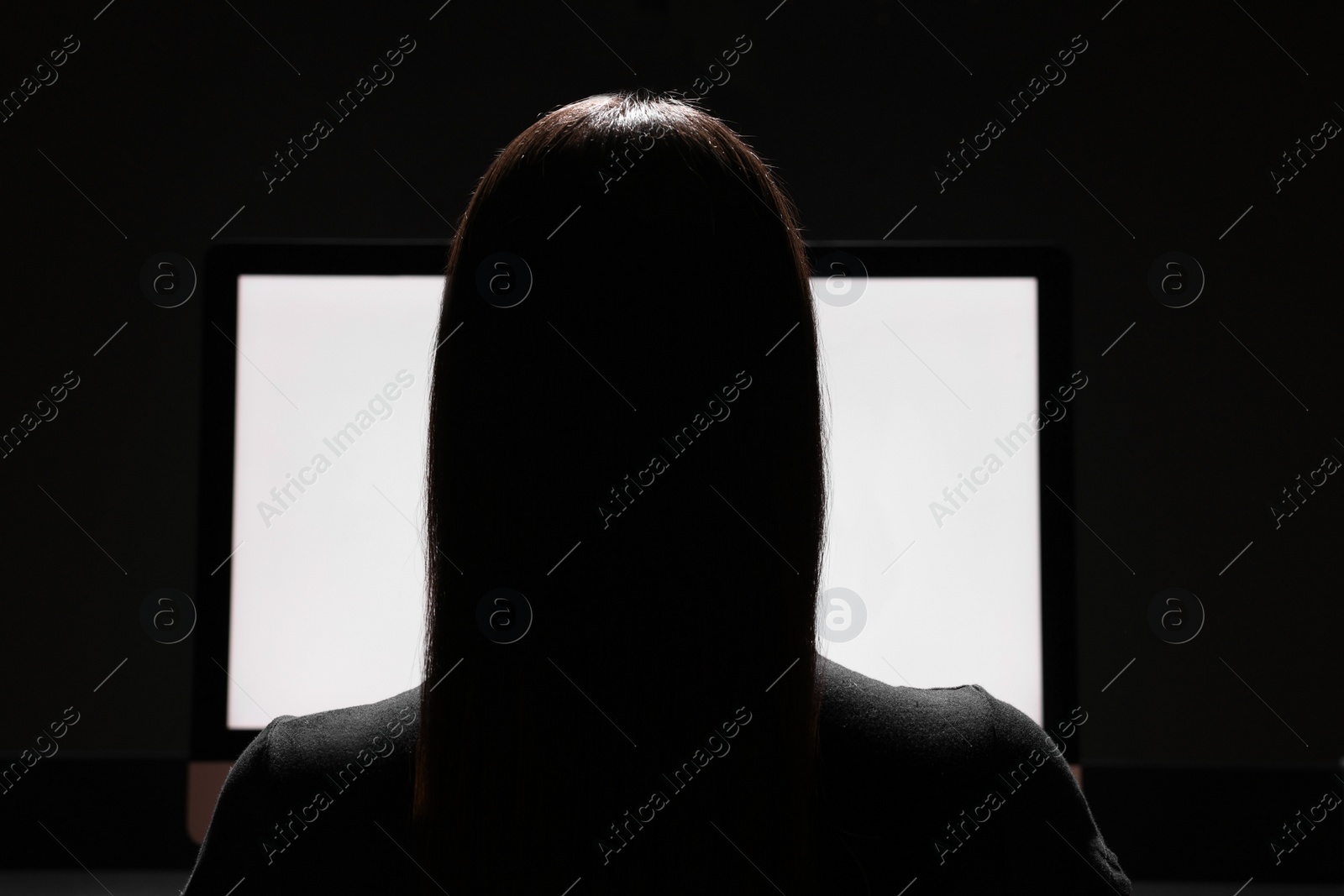 Photo of Woman using computer in dark room, back view. Internet addiction