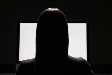 Photo of Woman using computer in dark room, back view. Internet addiction