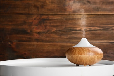 Photo of Modern essential oil diffuser on white table against wooden background. Space for text