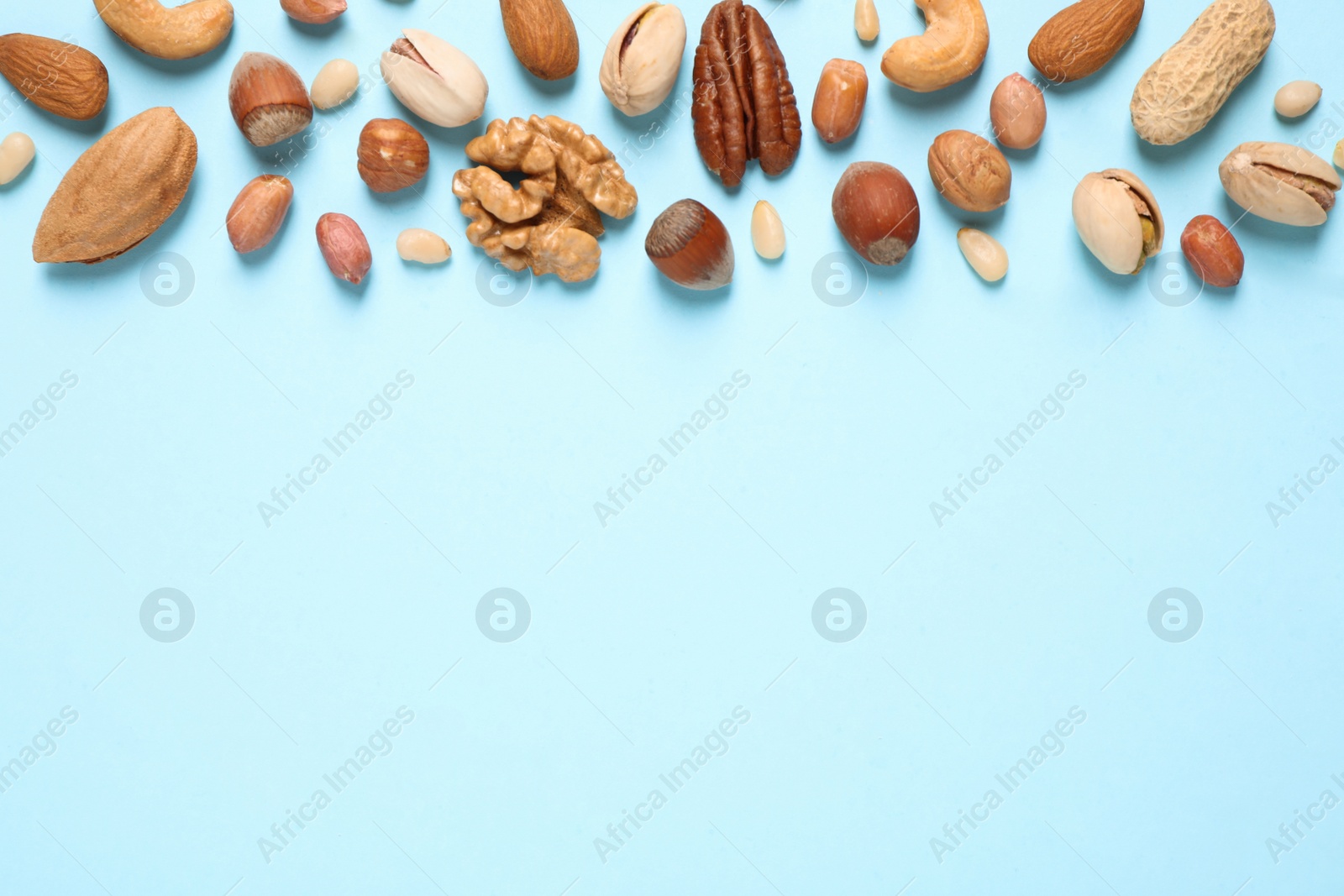 Photo of Different delicious nuts on light blue background, flat lay. Space for text