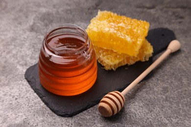 Sweet golden honey in jar, dipper and pieces of honeycomb on grey textured table