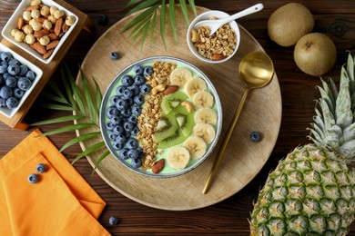 Photo of Tasty smoothie bowl with fresh fruits and oatmeal served on wooden table, flat lay