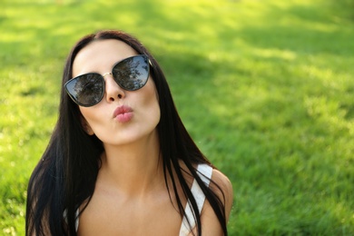 Beautiful young woman wearing stylish sunglasses in park. Space for text