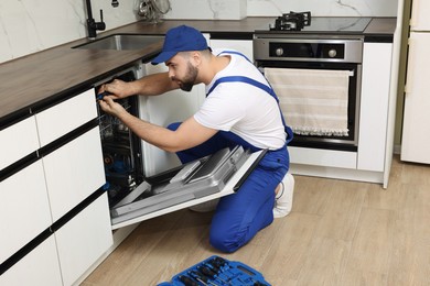 Serviceman repairing dishwasher with screwdriver in kitchen