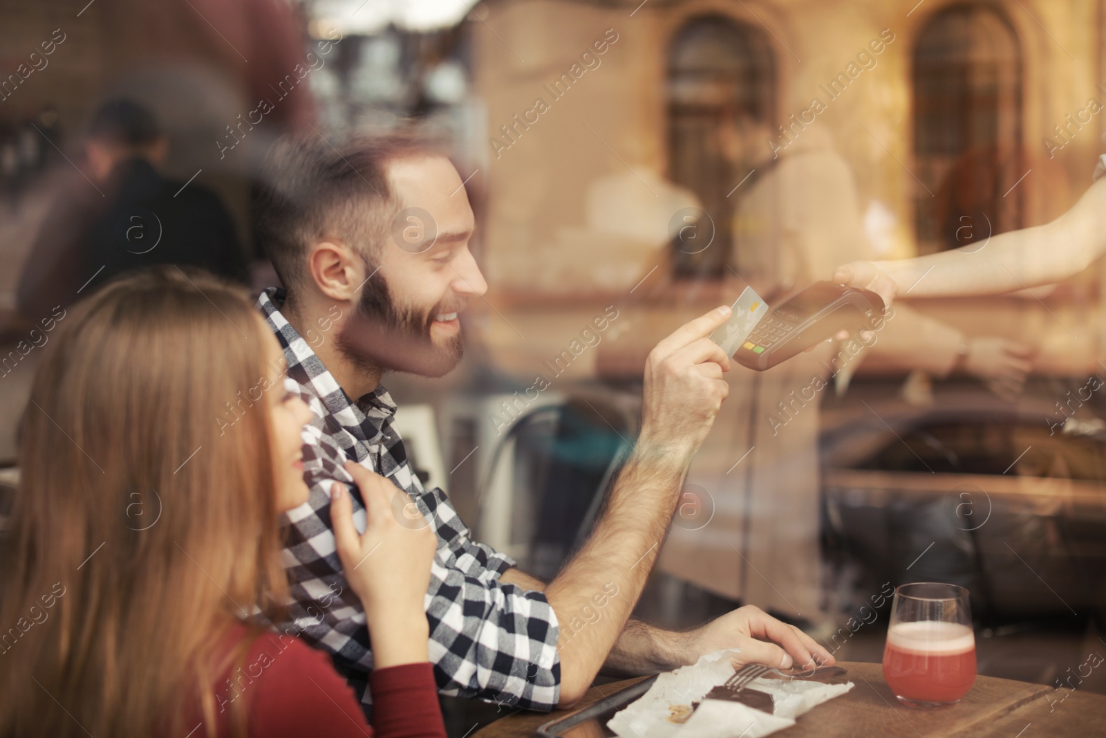 Photo of Man with credit card using payment terminal at restaurant, view through window