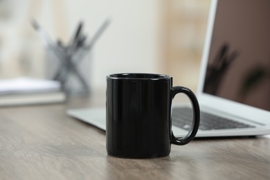 Black ceramic mug and laptop on wooden table indoors. Space for text