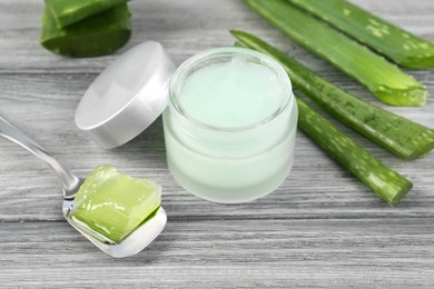 Photo of Jar with natural gel, spoon of peeled aloe vera and green leaves on light grey wooden table