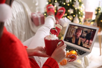 Photo of MYKOLAIV, UKRAINE - DECEMBER 25, 2020: Woman with sweet drink watching Home Alone movie on laptop indoors, closeup. Cozy winter holidays atmosphere