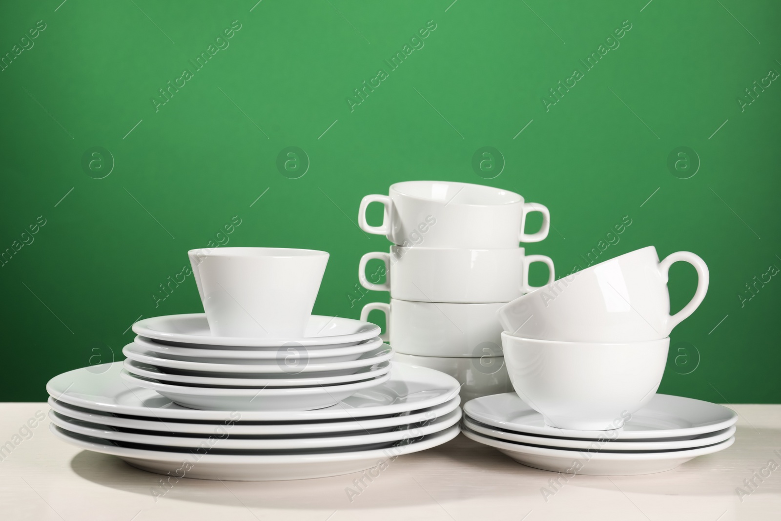 Photo of Set of clean dishware on white table against green background