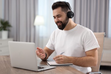 Young man in headphones using video chat during webinar at table in room