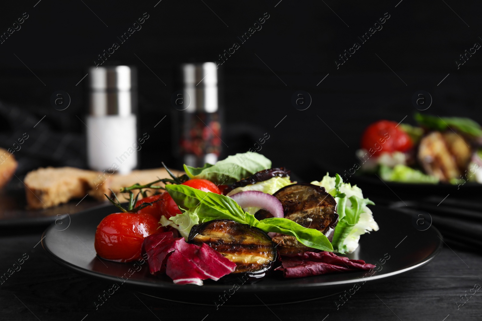 Photo of Delicious salad with roasted eggplant and basil served on black wooden table