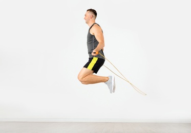 Young sportive man training with jump rope in light room
