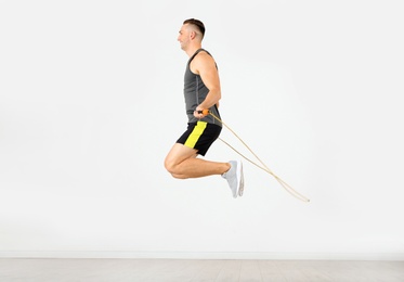 Photo of Young sportive man training with jump rope in light room