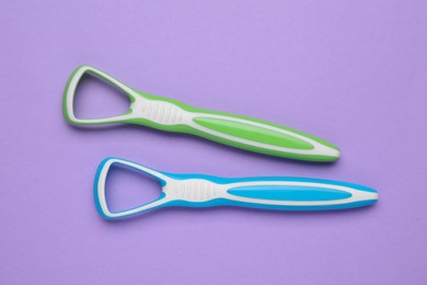 Colorful tongue cleaners on violet background, flat lay