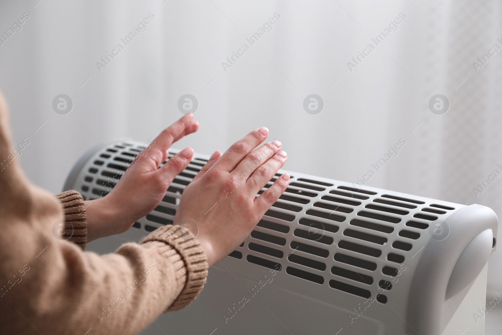 Photo of Woman warming hands near electric heater at home, closeup