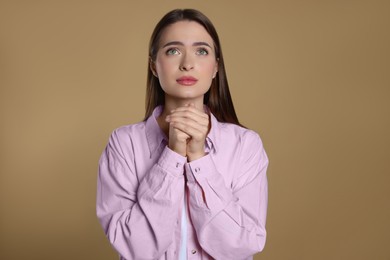 Woman with clasped hands praying on beige background