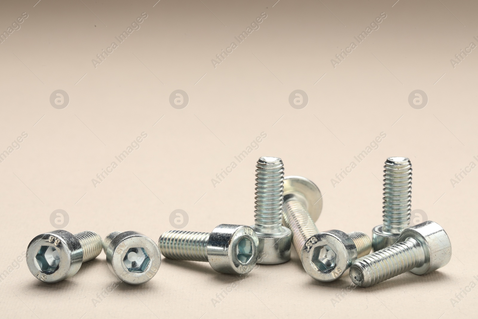 Photo of Many metal socket screws on beige background, closeup. Space for text