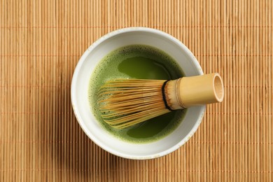 Photo of Cup of fresh green matcha tea with whisk on bamboo mat, top view