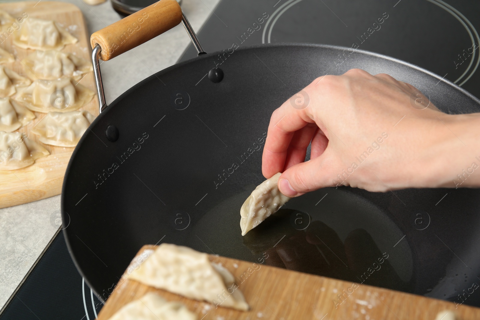 Photo of Woman putting raw gyoza on frying pan with hot oil, closeup