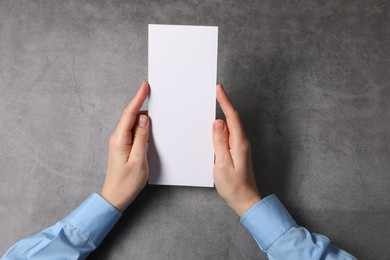 Woman holding blank card at grey table, top view. Mockup for design