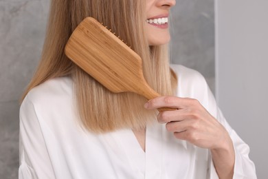 Photo of Woman in white robe brushing her hair indoors, closeup